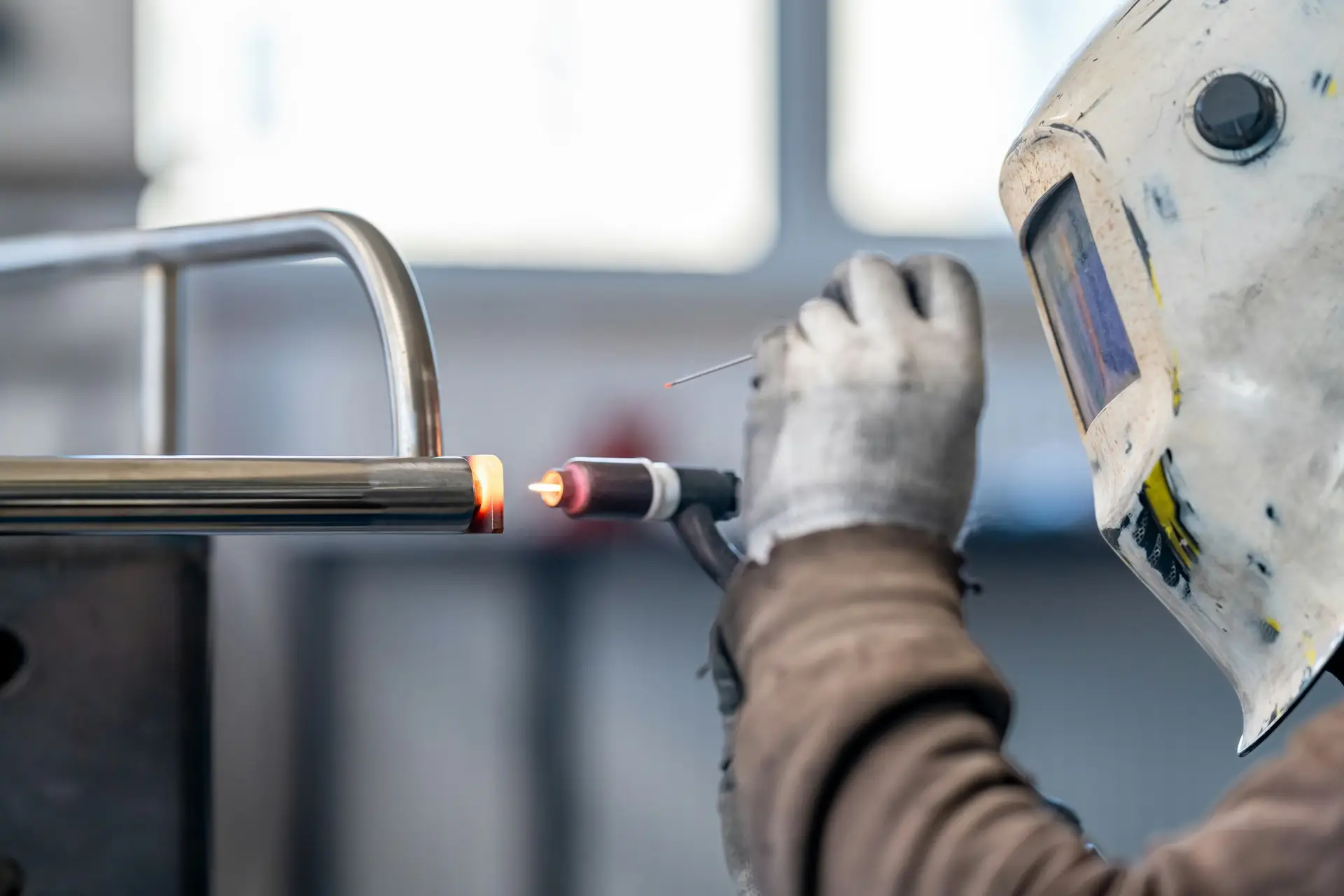 A man wearing a welding helmet is using a welding machine to weld a metal pipe